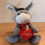 Peluche très mignonne avec un bandana rouge et tenant un coeur rouge avec écrit "Je t'aime"